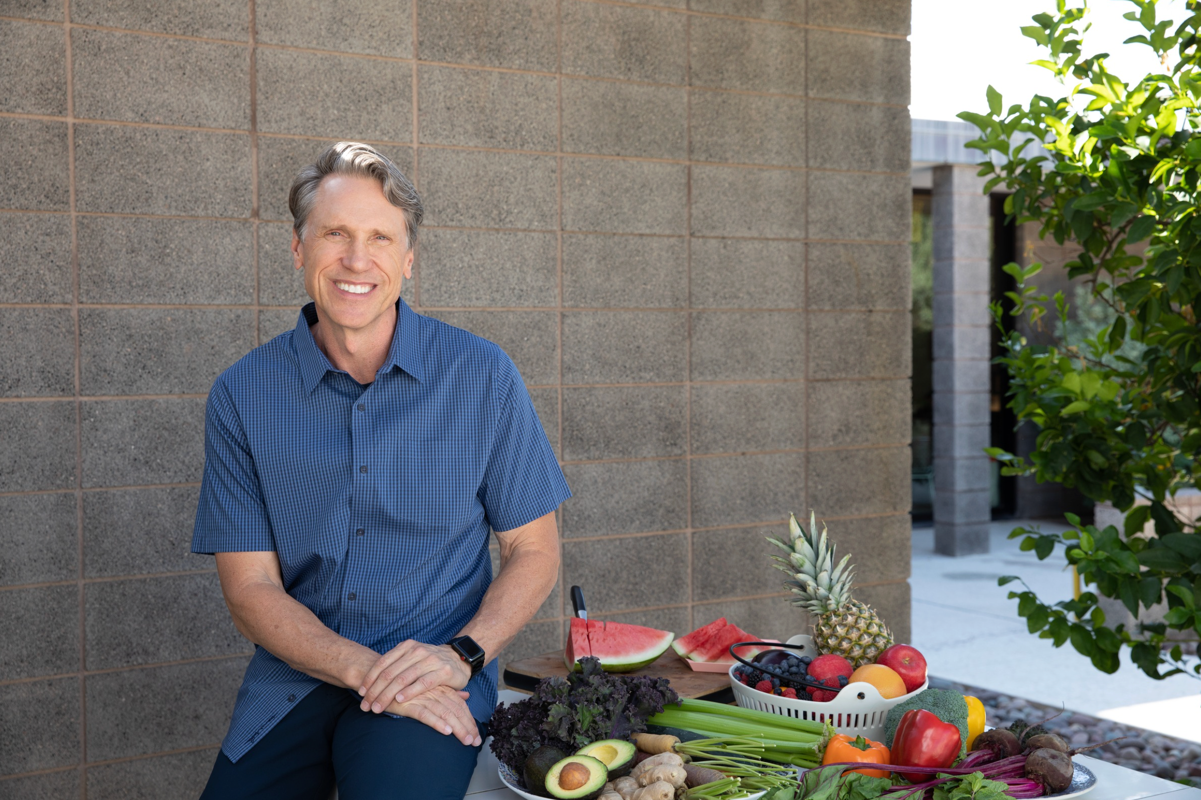 Dr. Murray outside wearing a blue shirt and sitting on a table with various fruits