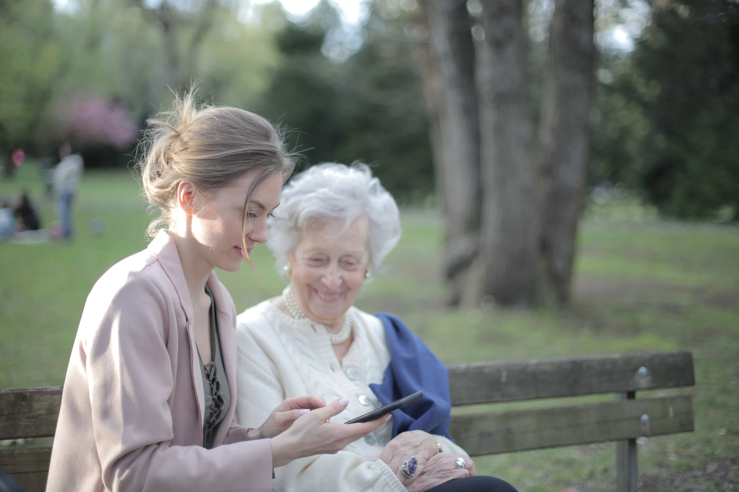A young and an elderly lady sitting on a park bench together looking at a mobile phone