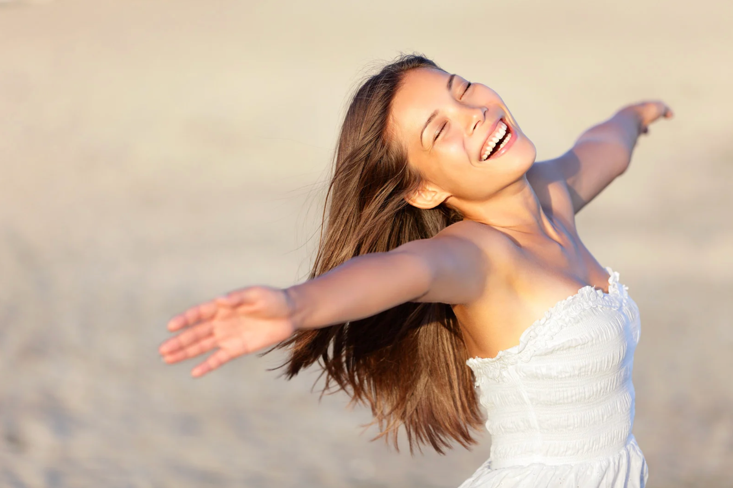 Young woman on beach stretching her arms out and smiling