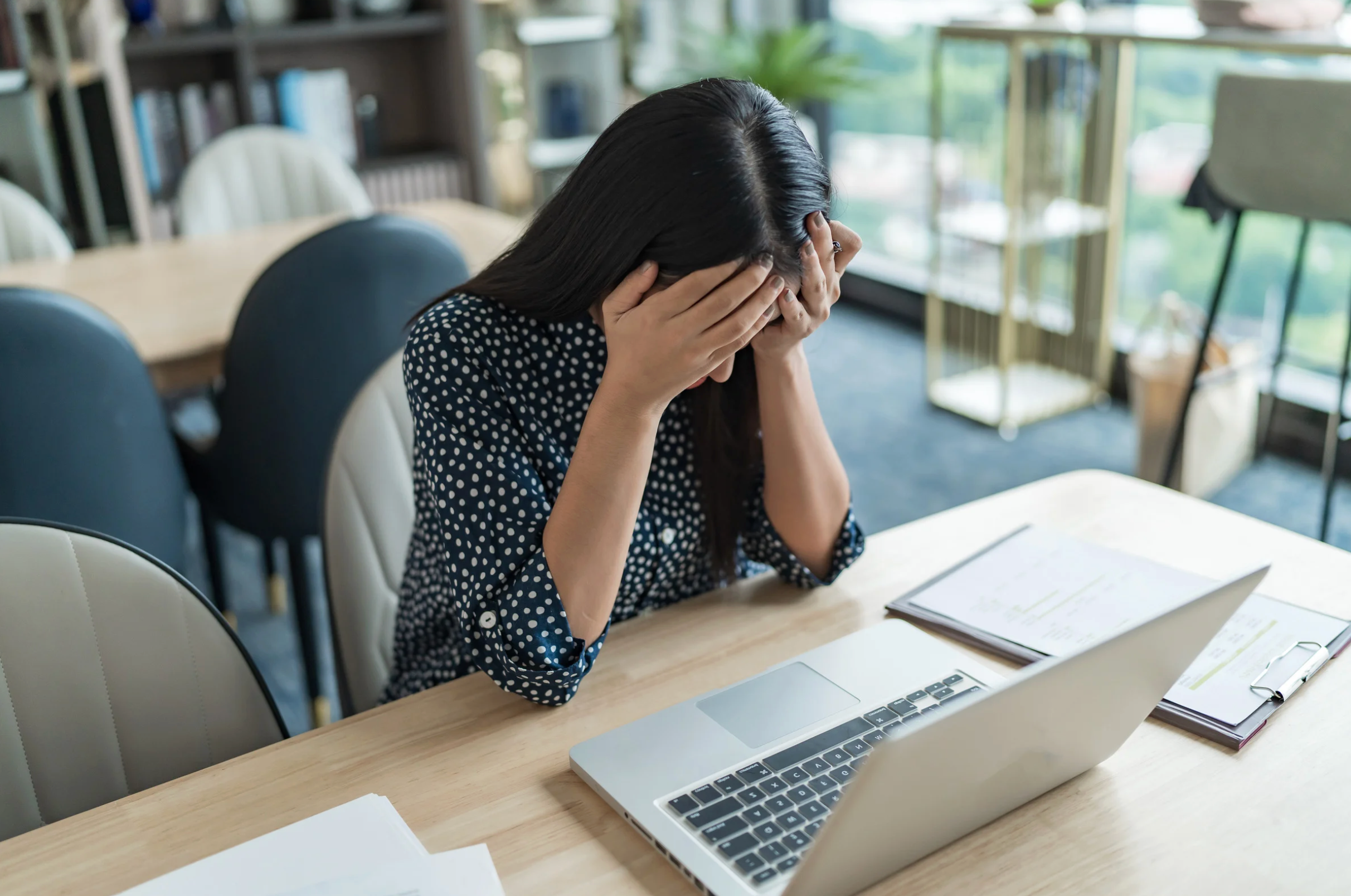Dark haired lading sitting at a desk with her head in hands