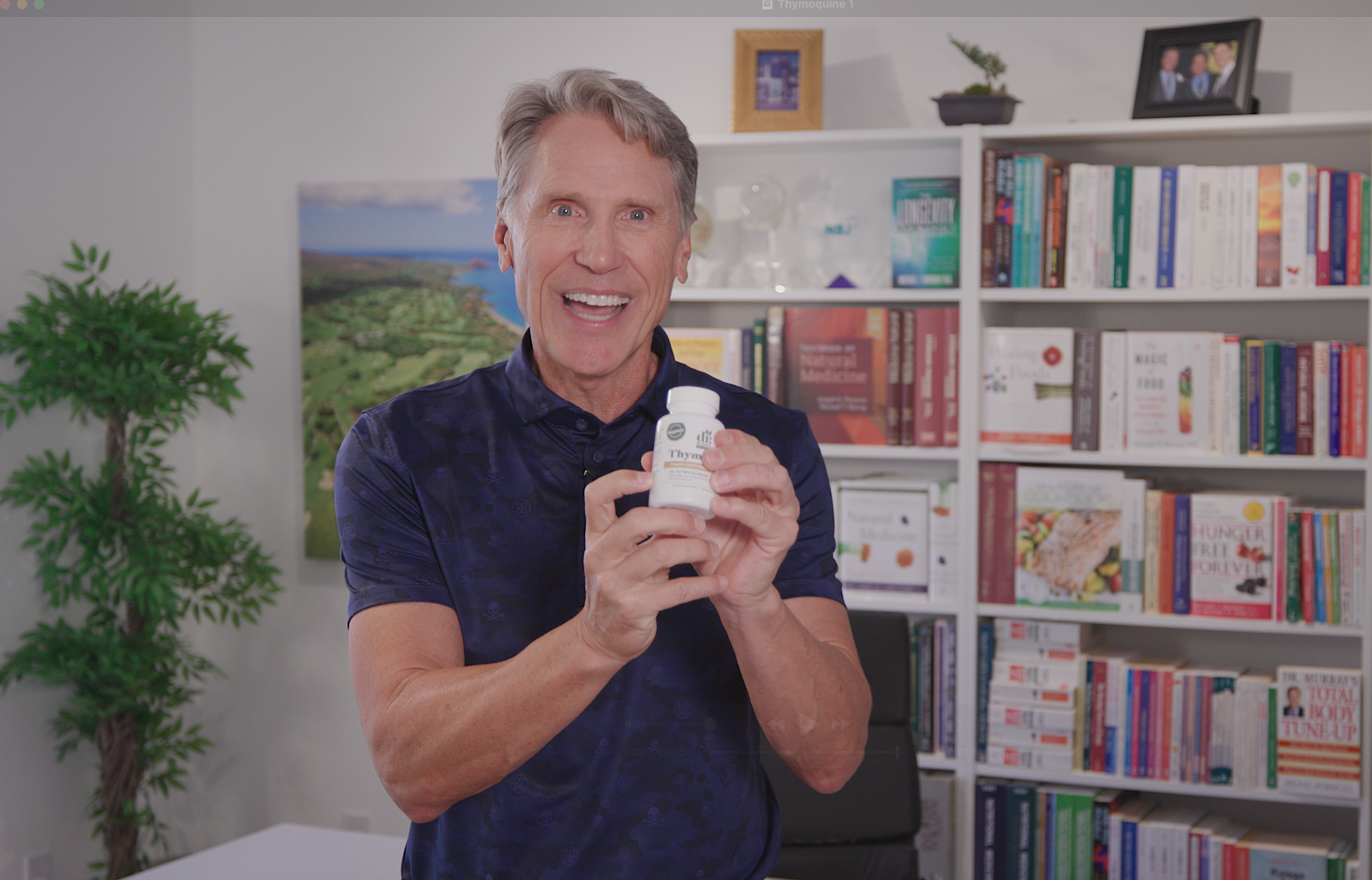Dr. Murray standing in front of shelves of book holding a bottle of ThymoQuin