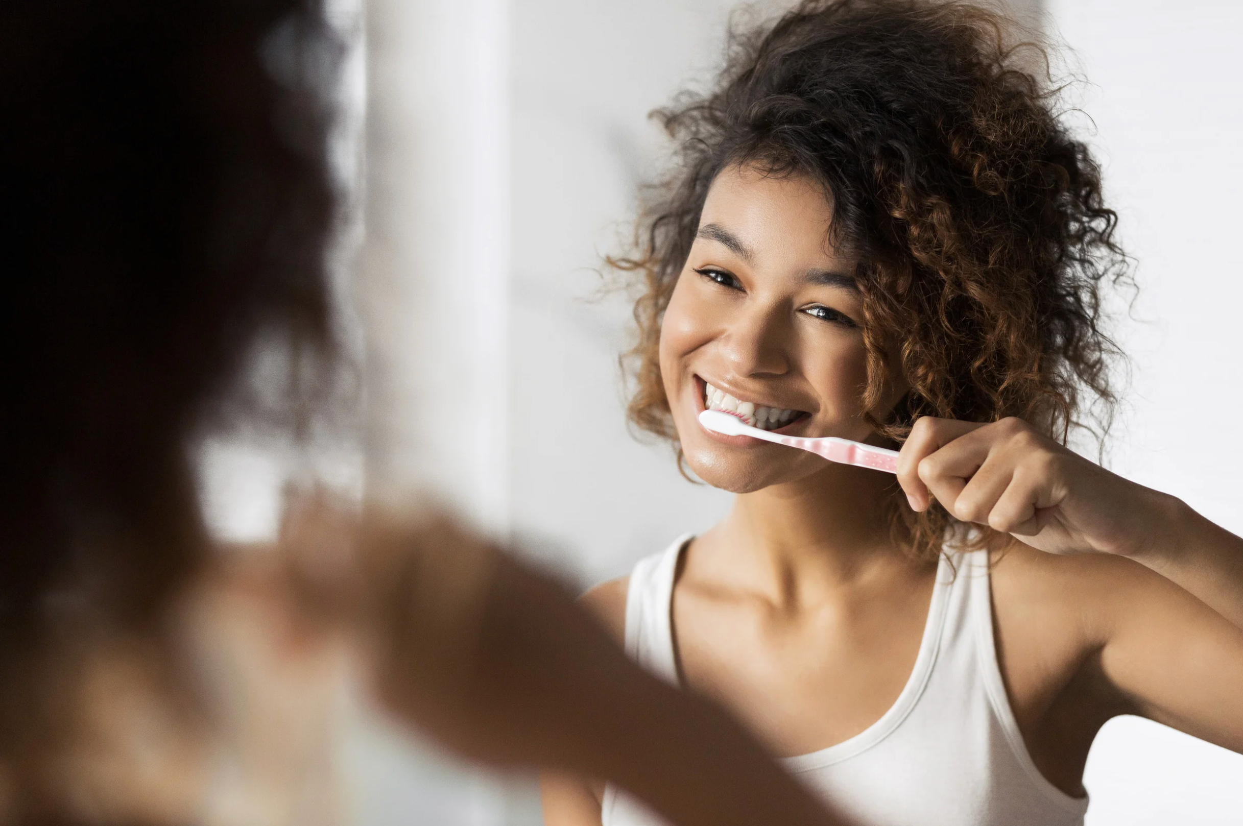 Young woman brushing her teeth in front of the mirror