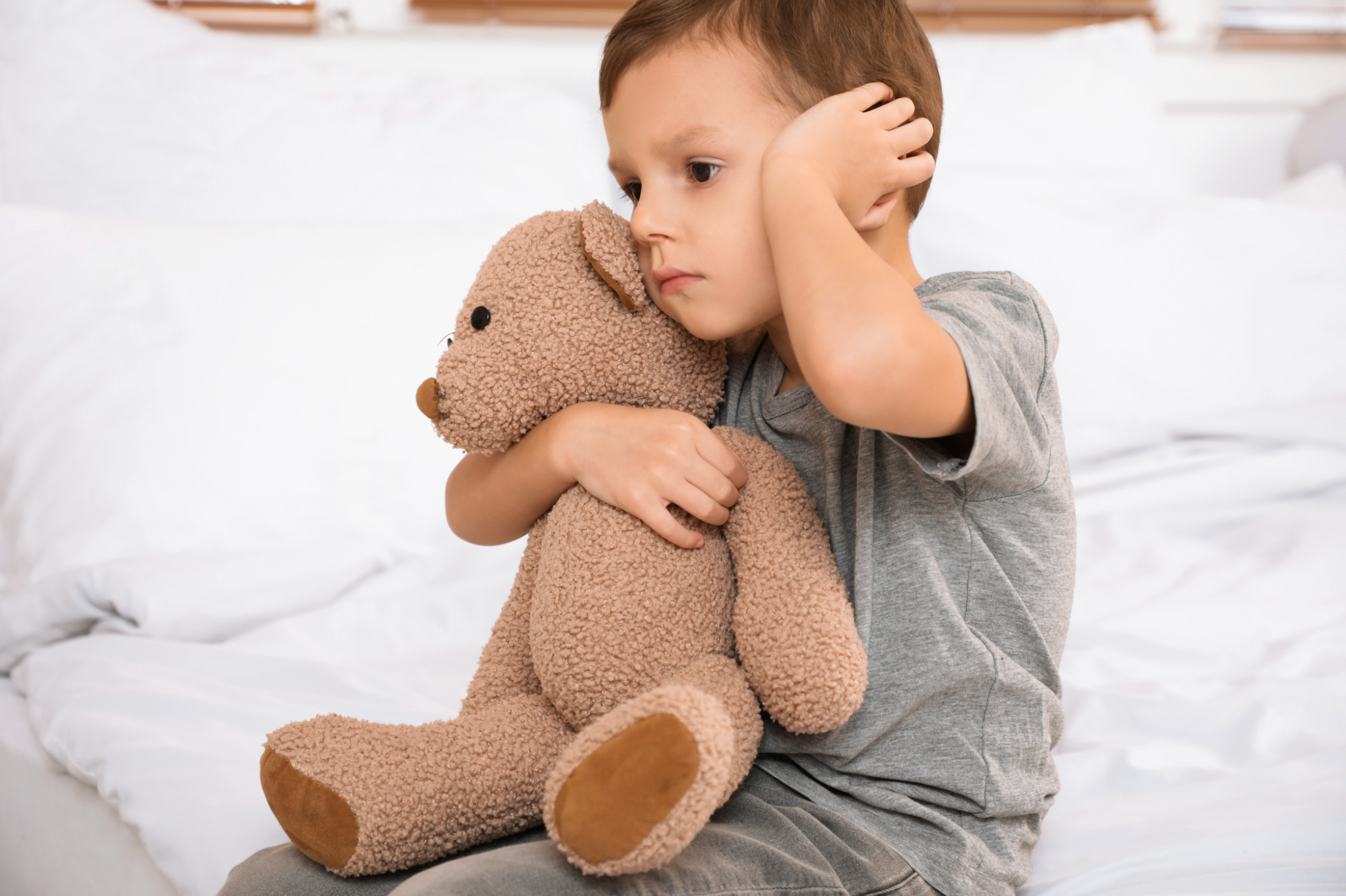 Young boy holding a teddy bear and covering his left hear with the other hand