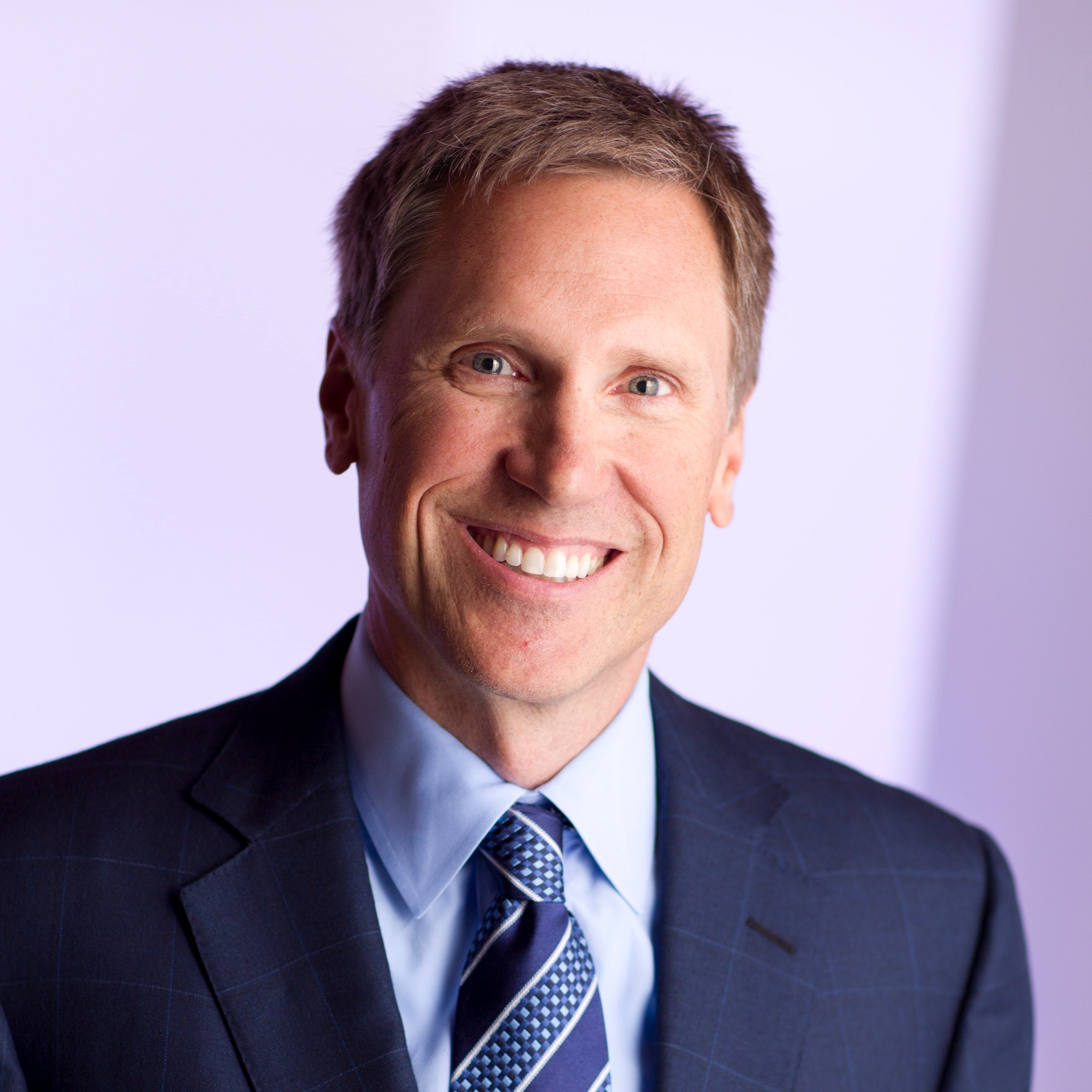 Dr. Murray wearing a suit and tie against a light purple background