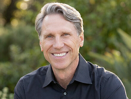 Dr. Murray with gray hair wearing a black shirt against a blurred green background