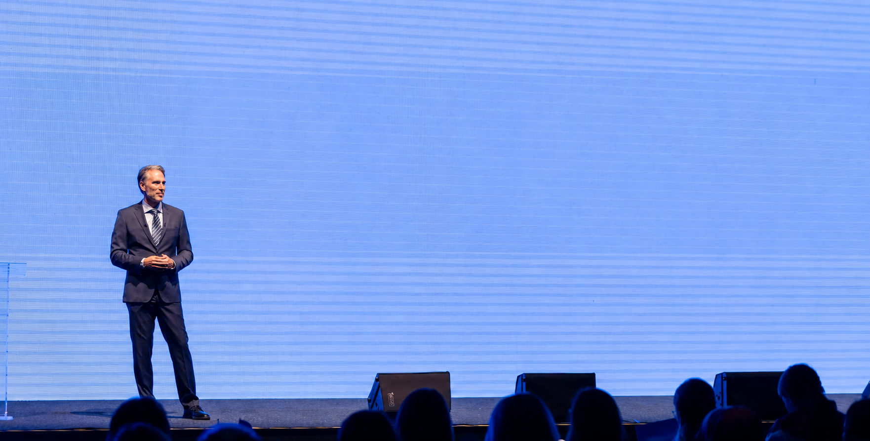 Dr. Michael T Murray in a suit standing on a stage with a blue screen background