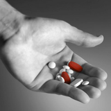 Hand holding a variety of pills with a gray background